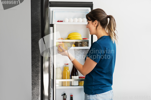 Image of happy woman taking food from fridge at home