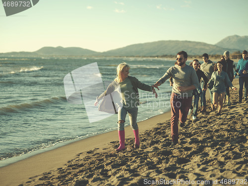 Image of Group of friends running on beach during autumn day