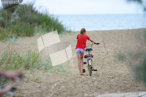 Image of Girl drags a bicycle on the sand at the seaside