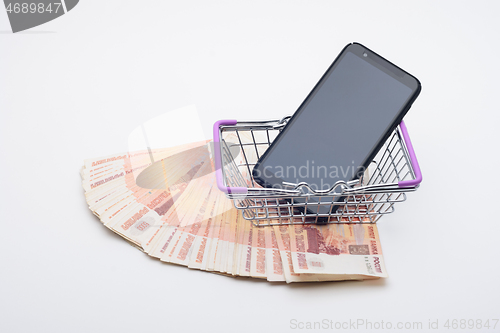 Image of Against the background of five thousandth bills is a grocery basket with a cell phone