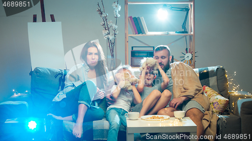 Image of Happy family watching projector, TV, movies with popcorn in the evening at home. Mother, father and kids spending time together.