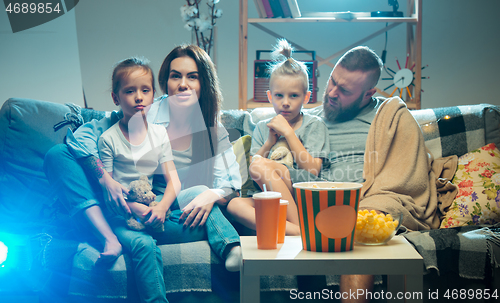 Image of Happy family watching projector, TV, movies with popcorn in the evening at home. Mother, father and kids spending time together.