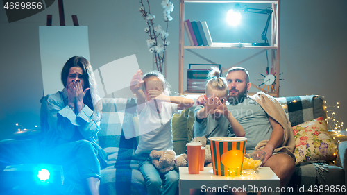 Image of Happy family watching projector, TV, movies with popcorn in the evening at home. Mother, father and kids spending time together.