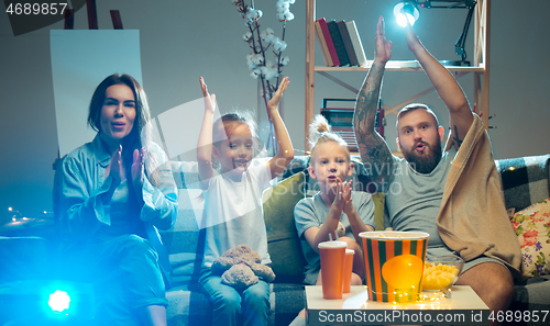 Image of Happy family watching projector, TV, movies with popcorn in the evening at home. Mother, father and kids spending time together.