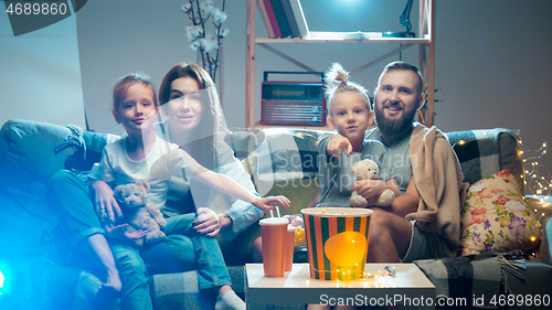 Image of Happy family watching projector, TV, movies with popcorn in the evening at home. Mother, father and kids spending time together.