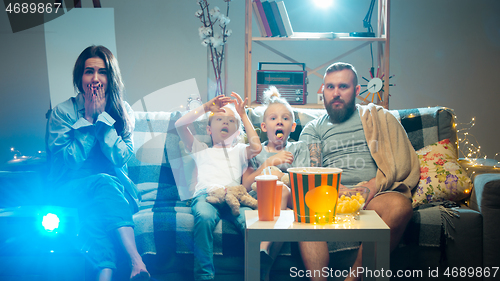 Image of Happy family watching projector, TV, movies with popcorn in the evening at home. Mother, father and kids spending time together.