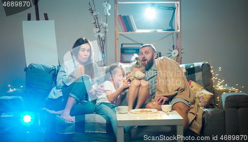 Image of Happy family watching projector, TV, movies with popcorn in the evening at home. Mother, father and kids spending time together.