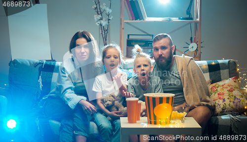 Image of Happy family watching projector, TV, movies with popcorn in the evening at home. Mother, father and kids spending time together.