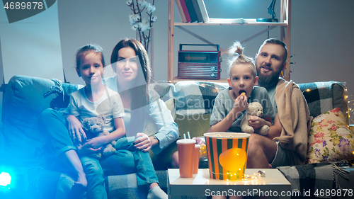 Image of Happy family watching projector, TV, movies with popcorn in the evening at home. Mother, father and kids spending time together.