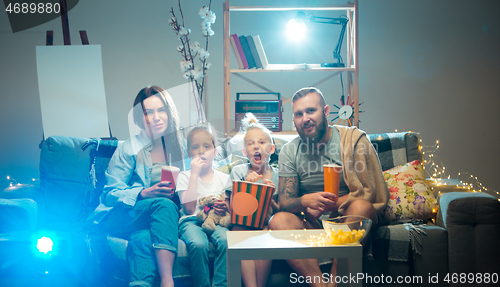 Image of Happy family watching projector, TV, movies with popcorn in the evening at home. Mother, father and kids spending time together.