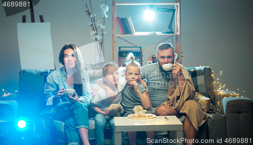 Image of Happy family watching projector, TV, movies with popcorn in the evening at home. Mother, father and kids spending time together.