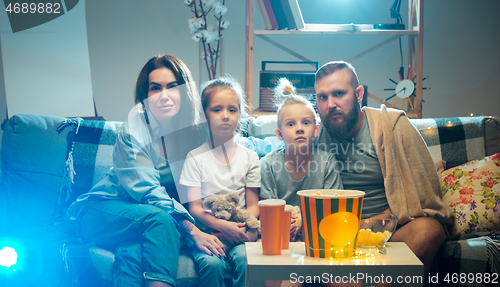 Image of Happy family watching projector, TV, movies with popcorn in the evening at home. Mother, father and kids spending time together.