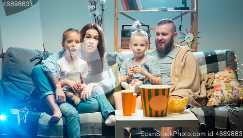 Image of Happy family watching projector, TV, movies with popcorn in the evening at home. Mother, father and kids spending time together.