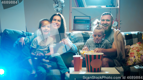 Image of Happy family watching projector, TV, movies with popcorn in the evening at home. Mother, father and kids spending time together.