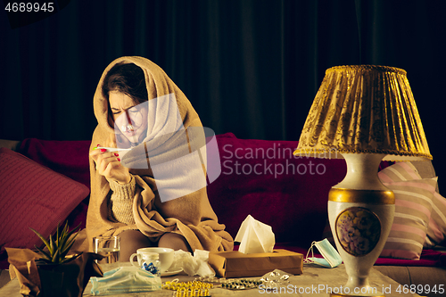 Image of Woman wrapped in a plaid looks sick, ill, sneezing and coughing sitting at home indoors