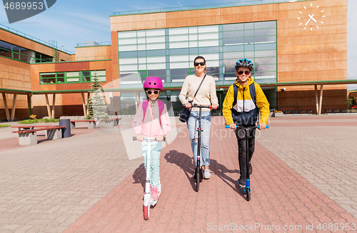 Image of happy school children with mother riding scooters