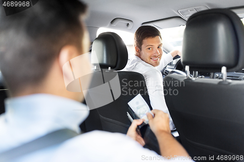 Image of male car driver looking at passenger with money