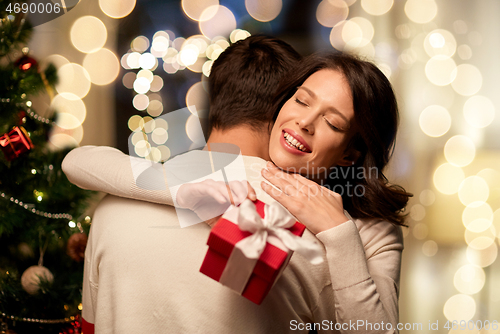 Image of happy couple with christmas gift hugging at home