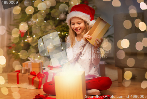 Image of smiling girl in santa hat opening christmas gift