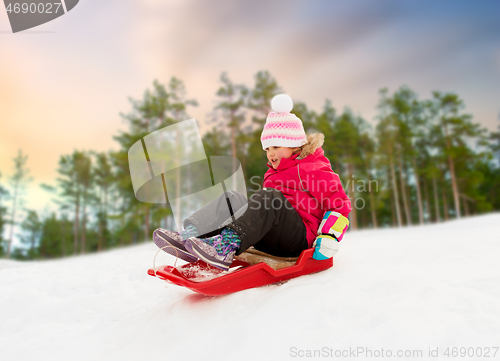 Image of happy little girl sliding down on sled in winter