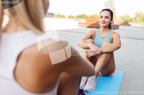 Image of happy women sitting on exercise mats outdoors