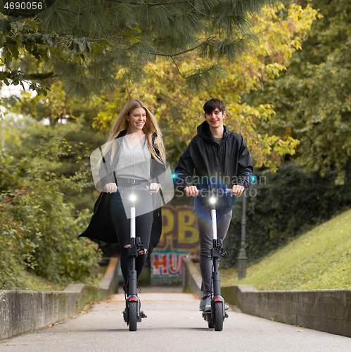 Image of Trendy fashinable teenagers riding public rental electric scooters in urban city park. New eco-friendly modern public city transport in Ljubljana, Slovenia