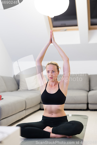 Image of Beautiful blonde woman doing home workout indoors. Woman practice yoga at home. Fit girl using workout tutorials for healthy active lifestyle. Woman using quarantine for home workouts.