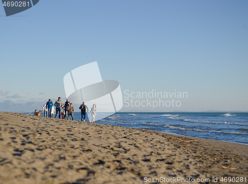 Image of Group of friends running on beach during autumn day