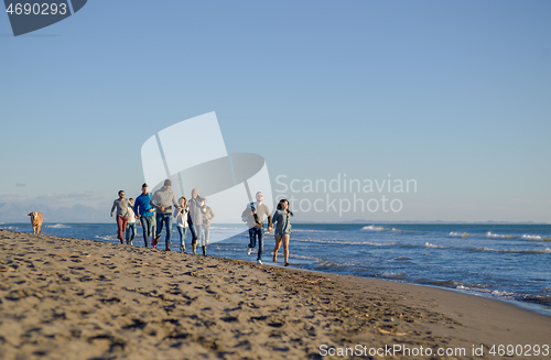 Image of Group of friends running on beach during autumn day