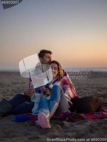 Image of Loving Young Couple Sitting On The Beach beside Campfire drinkin