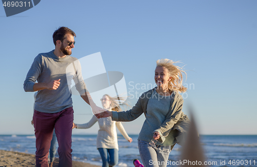 Image of Group of friends running on beach during autumn day