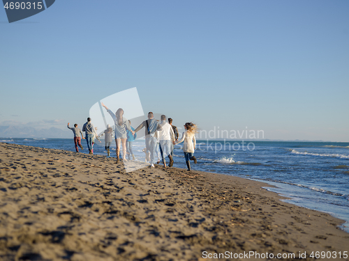 Image of Group of friends running on beach during autumn day