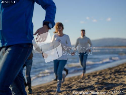 Image of Group of friends running on beach during autumn day