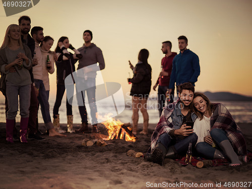 Image of Couple enjoying bonfire with friends on beach