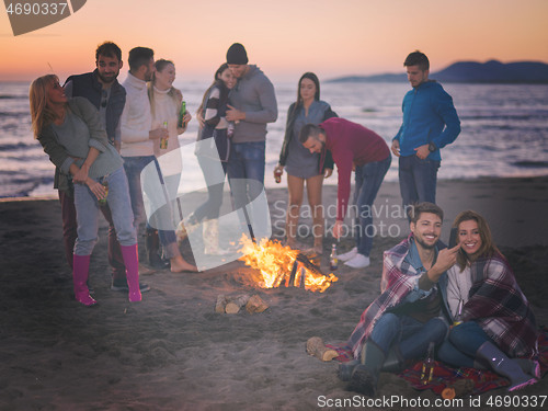 Image of Couple enjoying bonfire with friends on beach