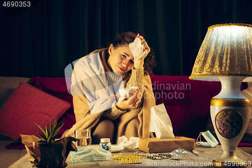 Image of Woman wrapped in a plaid looks sick, ill, sneezing and coughing sitting at home indoors