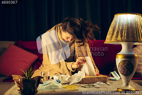 Image of Woman wrapped in a plaid looks sick, ill, sneezing and coughing sitting at home indoors