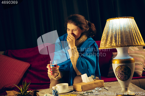 Image of Woman wrapped in a plaid looks sick, ill, sneezing and coughing sitting at home indoors