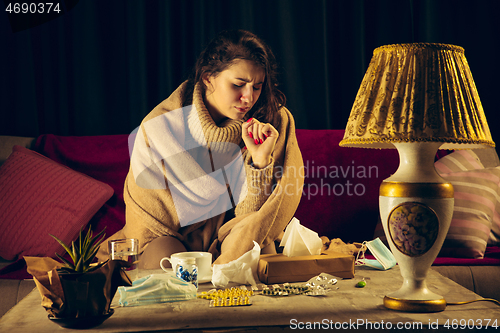 Image of Woman wrapped in a plaid looks sick, ill, sneezing and coughing sitting at home indoors