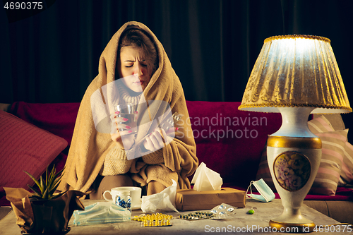 Image of Woman wrapped in a plaid looks sick, ill, sneezing and coughing sitting at home indoors