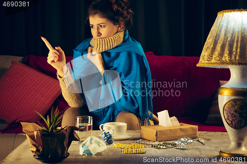 Image of Woman wrapped in a plaid looks sick, ill, sneezing and coughing sitting at home indoors