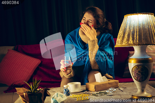 Image of Woman wrapped in a plaid looks sick, ill, sneezing and coughing sitting at home indoors