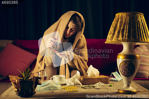 Image of Woman wrapped in a plaid looks sick, ill, sneezing and coughing sitting at home indoors