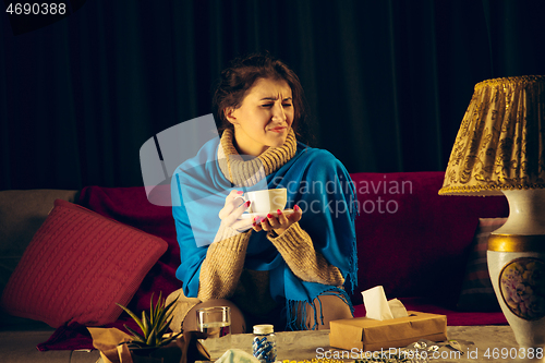 Image of Woman wrapped in a plaid looks sick, ill, sneezing and coughing sitting at home indoors