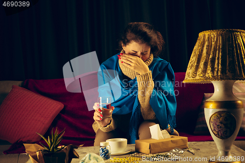 Image of Woman wrapped in a plaid looks sick, ill, sneezing and coughing sitting at home indoors