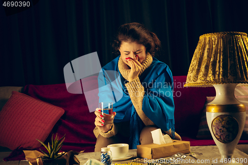 Image of Woman wrapped in a plaid looks sick, ill, sneezing and coughing sitting at home indoors