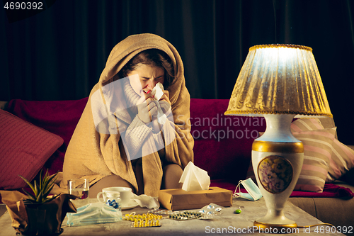 Image of Woman wrapped in a plaid looks sick, ill, sneezing and coughing sitting at home indoors