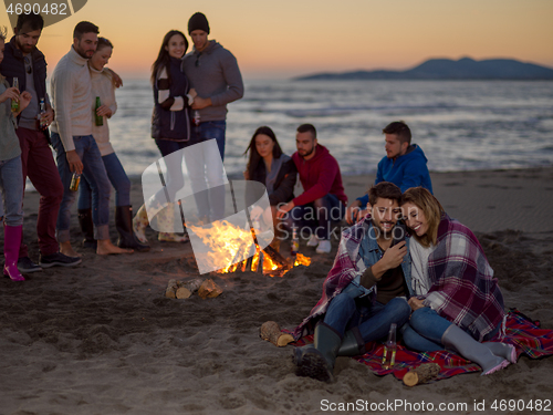 Image of Couple enjoying bonfire with friends on beach