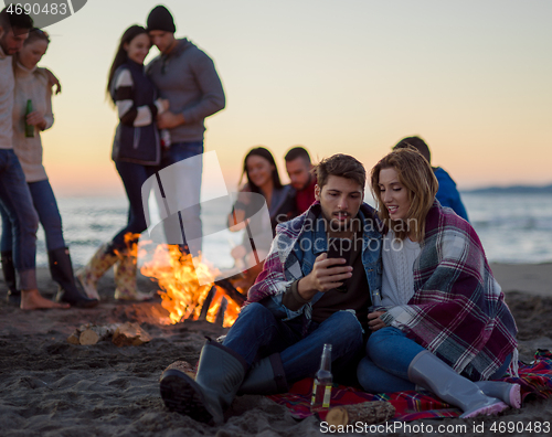 Image of Couple enjoying bonfire with friends on beach