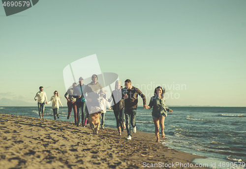 Image of Group of friends running on beach during autumn day